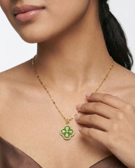 Woman wearing a gold necklace with a green pendant on a plain background
