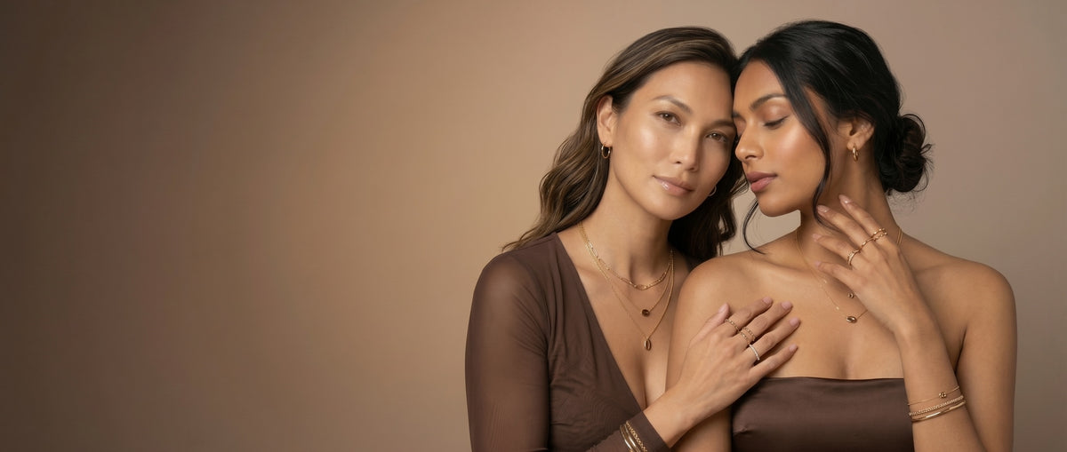 Two women wearing layered gold plated necklaces, bangles and stacked rings