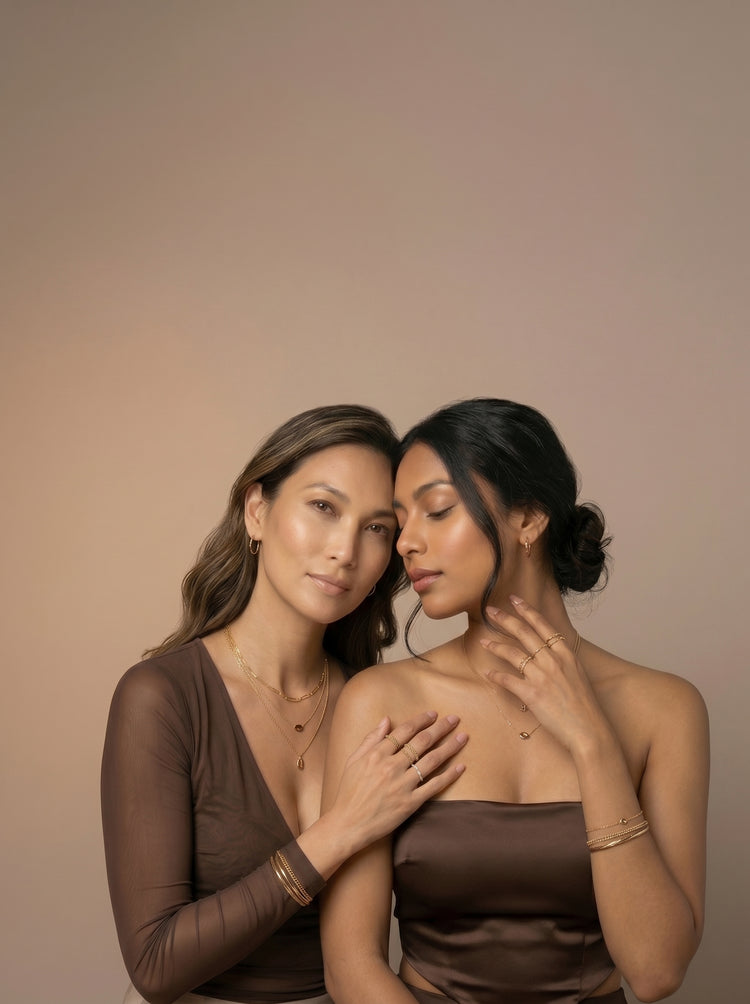 Two women wearing layered gold plated necklaces, bangles and stacked rings